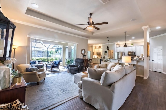 living area with a tray ceiling, dark wood finished floors, and a ceiling fan