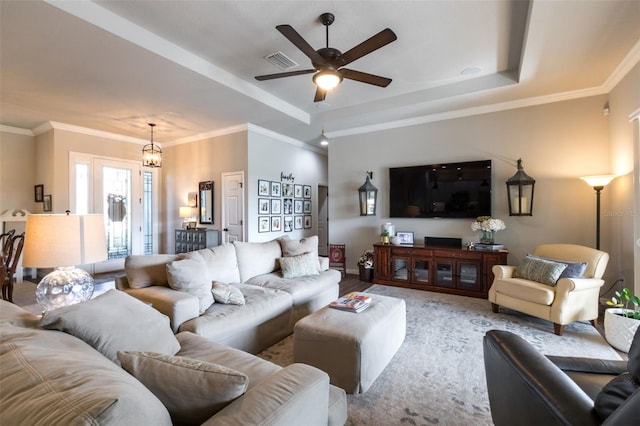 living area featuring ornamental molding, a raised ceiling, visible vents, and ceiling fan with notable chandelier