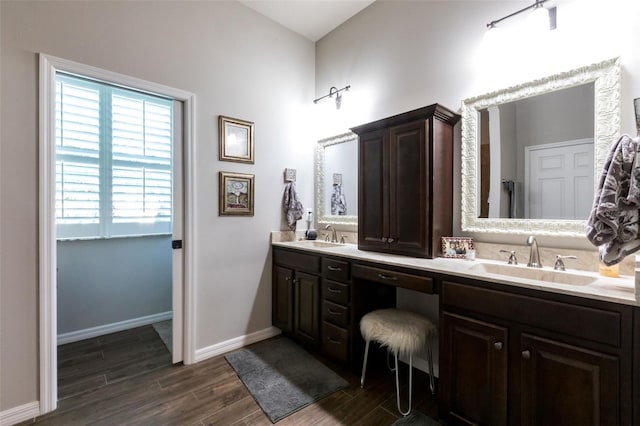 bathroom with double vanity, wood finished floors, a sink, and baseboards