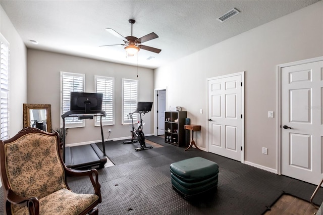 exercise area featuring a ceiling fan, visible vents, a textured ceiling, and baseboards