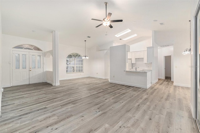 unfurnished living room with ceiling fan with notable chandelier, light hardwood / wood-style floors, sink, and high vaulted ceiling