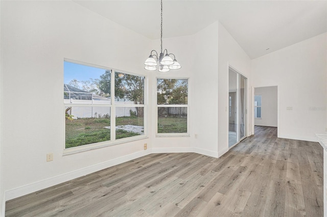 unfurnished dining area featuring an inviting chandelier, high vaulted ceiling, and light hardwood / wood-style flooring