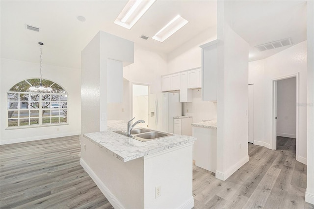 kitchen featuring kitchen peninsula, vaulted ceiling, sink, white cabinets, and white fridge with ice dispenser