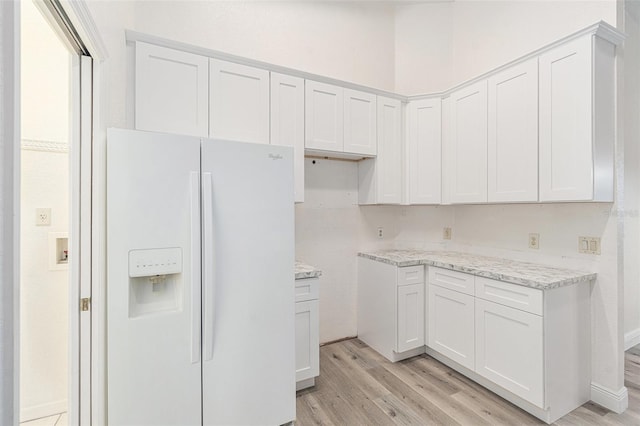 kitchen featuring white refrigerator with ice dispenser, white cabinets, light hardwood / wood-style flooring, and light stone counters