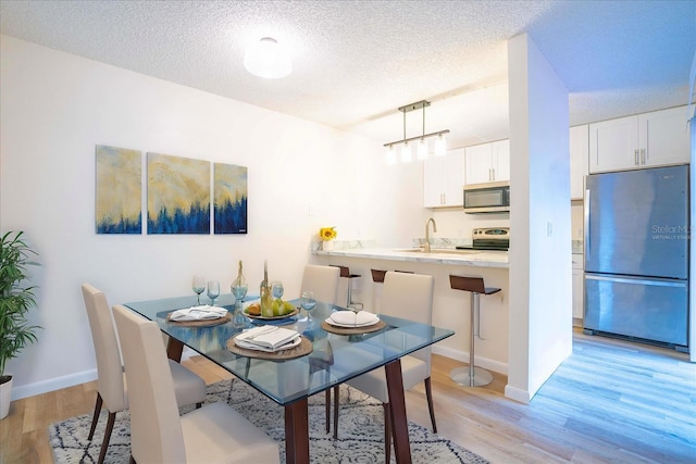 dining area featuring sink, a textured ceiling, and light wood-type flooring