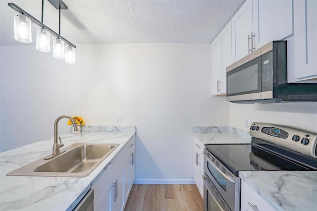 kitchen with pendant lighting, appliances with stainless steel finishes, a textured ceiling, white cabinetry, and sink