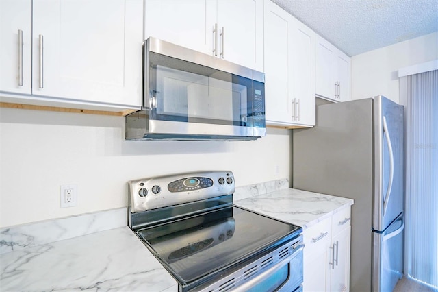 kitchen with a textured ceiling, appliances with stainless steel finishes, white cabinetry, and light stone counters