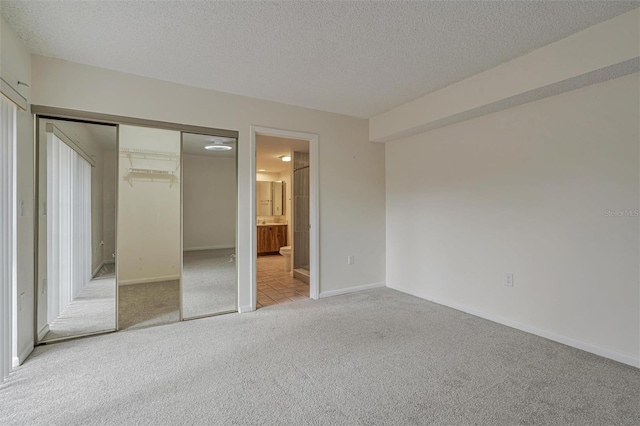 unfurnished bedroom featuring light colored carpet, a textured ceiling, a closet, and ensuite bath