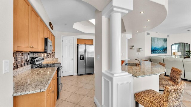 kitchen featuring stainless steel appliances, ornate columns, a tray ceiling, and light stone counters