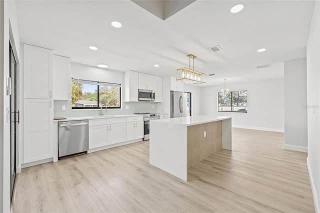 kitchen featuring stainless steel appliances, sink, pendant lighting, white cabinetry, and a kitchen island