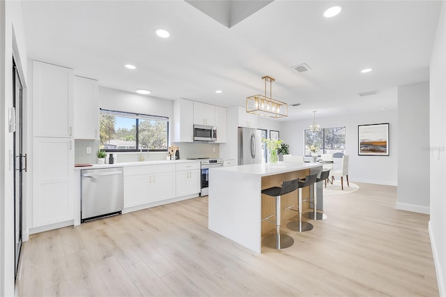 kitchen featuring white cabinetry, hanging light fixtures, stainless steel appliances, backsplash, and a kitchen island