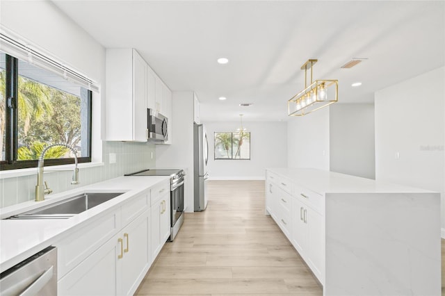 kitchen with appliances with stainless steel finishes, decorative light fixtures, white cabinetry, and sink