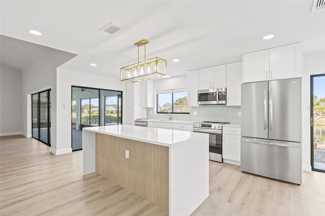 kitchen featuring decorative light fixtures, a kitchen island, white cabinetry, and appliances with stainless steel finishes