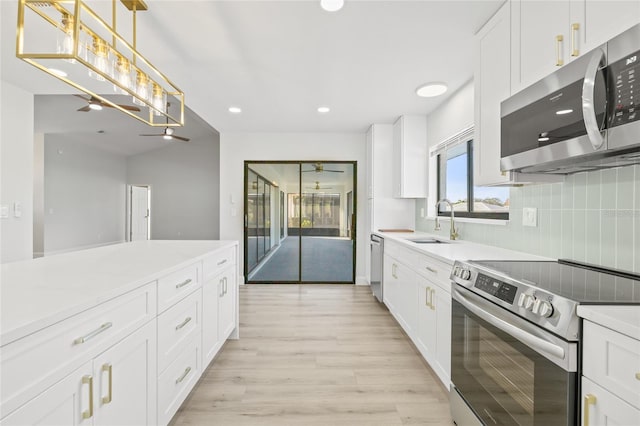 kitchen with white cabinets, sink, decorative light fixtures, light hardwood / wood-style floors, and stainless steel appliances