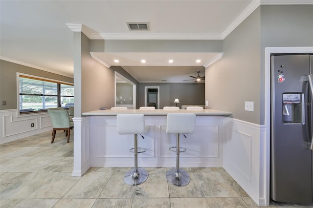 kitchen featuring a kitchen bar, kitchen peninsula, ornamental molding, ceiling fan, and stainless steel fridge with ice dispenser