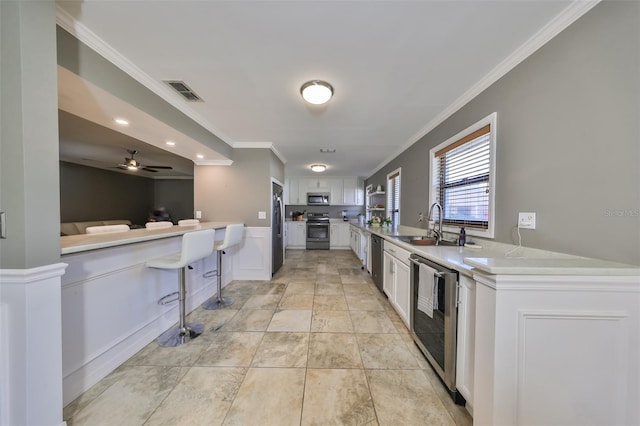 kitchen with kitchen peninsula, appliances with stainless steel finishes, a breakfast bar, ceiling fan, and white cabinetry