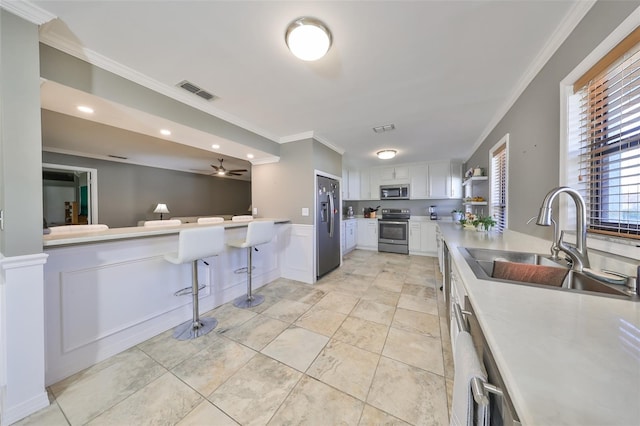 kitchen featuring ceiling fan, sink, a breakfast bar, white cabinets, and appliances with stainless steel finishes