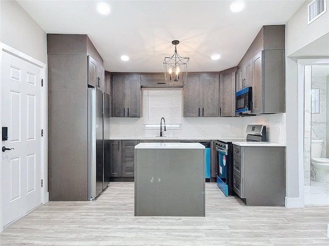 kitchen featuring appliances with stainless steel finishes, sink, pendant lighting, a chandelier, and a center island