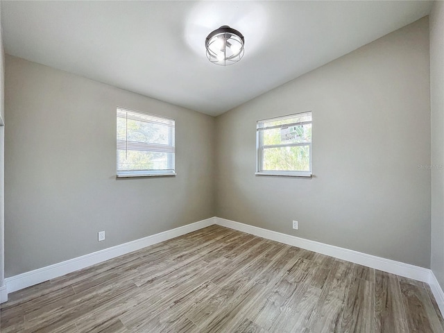 spare room featuring lofted ceiling, light hardwood / wood-style flooring, and a healthy amount of sunlight