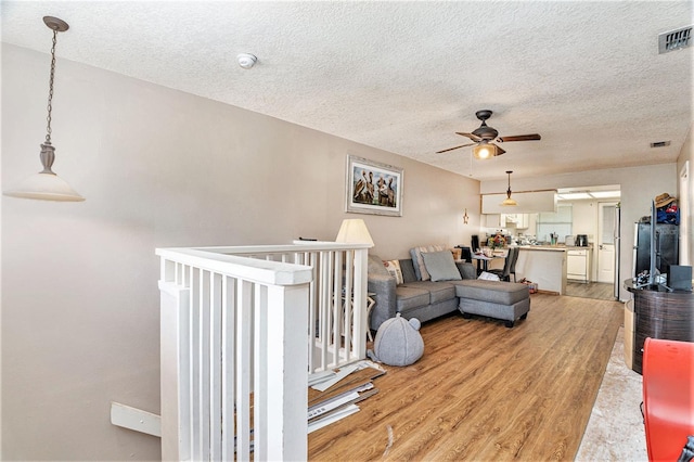 living room with hardwood / wood-style flooring, ceiling fan, and a textured ceiling