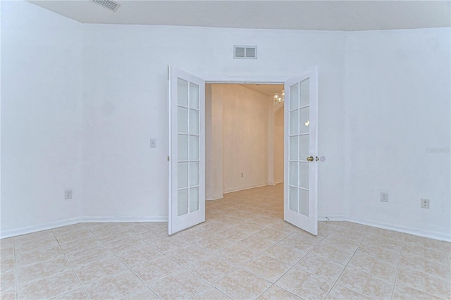 tiled empty room featuring french doors and a chandelier