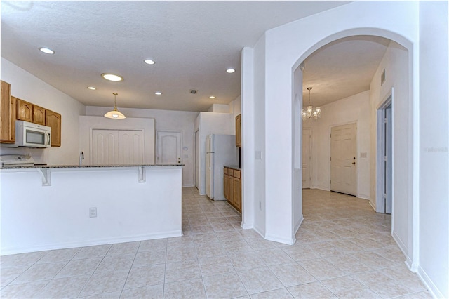 kitchen featuring dark stone counters, a breakfast bar, white appliances, a notable chandelier, and hanging light fixtures