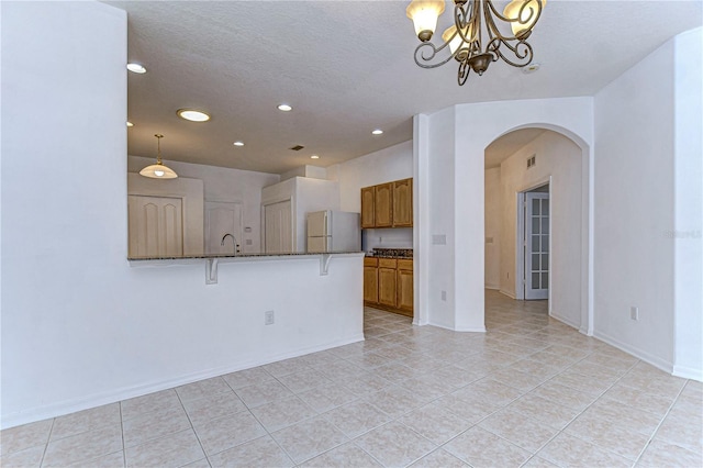 kitchen featuring a kitchen bar, dark stone counters, pendant lighting, white refrigerator, and an inviting chandelier