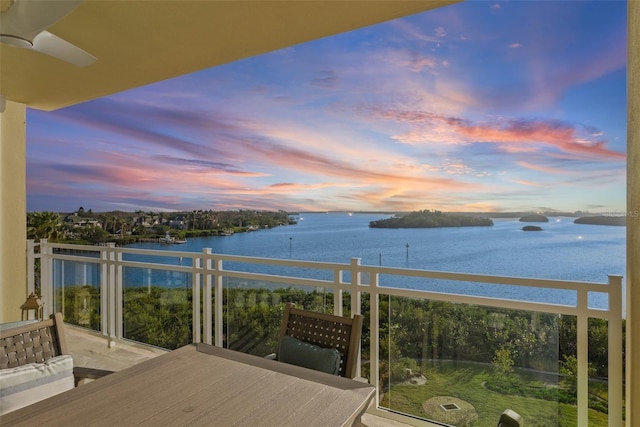 balcony at dusk with ceiling fan and a water view