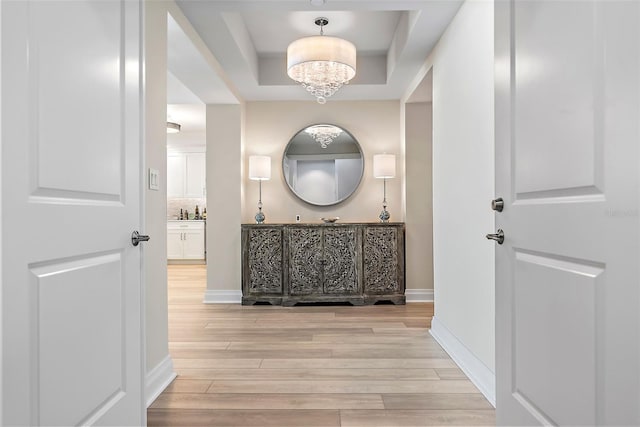 hallway featuring a tray ceiling, a chandelier, and light hardwood / wood-style floors