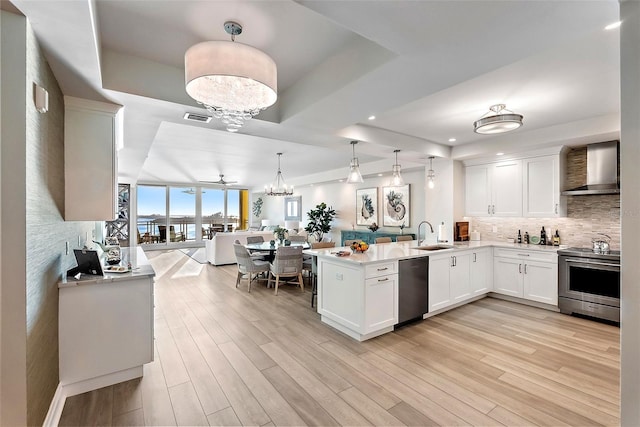 kitchen with white cabinets, a raised ceiling, wall chimney range hood, kitchen peninsula, and stainless steel appliances