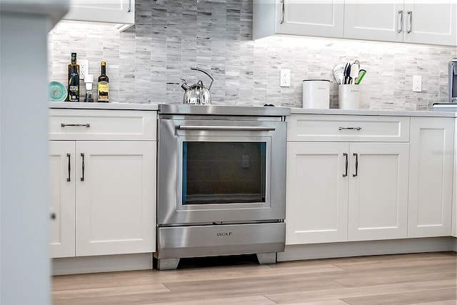 bar featuring stainless steel range, decorative backsplash, light hardwood / wood-style floors, and white cabinetry