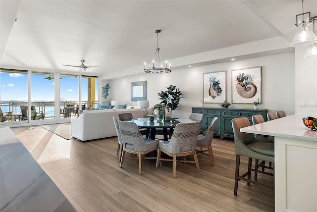 dining area with ceiling fan with notable chandelier, a water view, light hardwood / wood-style flooring, and floor to ceiling windows