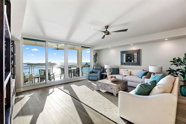 living room featuring ceiling fan, floor to ceiling windows, a water view, and wood-type flooring