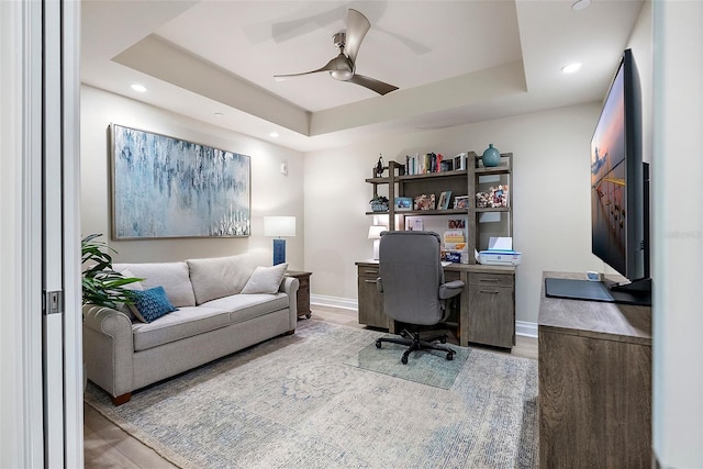 office space with light wood-type flooring, a raised ceiling, and ceiling fan