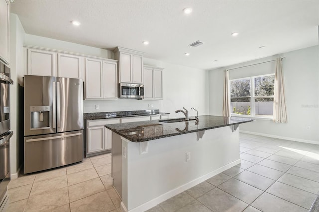 kitchen featuring sink, white cabinetry, dark stone counters, stainless steel appliances, and a kitchen island with sink