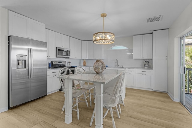465 Lake Murex Cir, Sanibel, FL 33957 - kitchen featuring white cabinetry, light stone counters, decorative light fixtures, appliances with stainless steel finishes, and light wood-type flooring