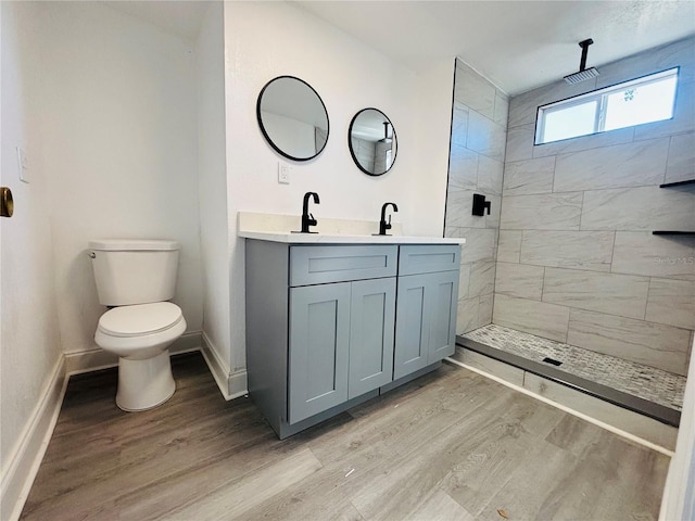 bathroom with toilet, tiled shower, wood-type flooring, and vanity