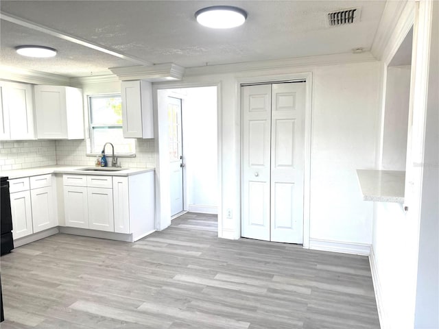 kitchen with white cabinets, decorative backsplash, sink, light wood-type flooring, and crown molding