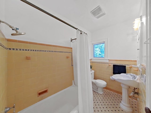 bathroom with tile walls, shower / tub combo with curtain, and toilet