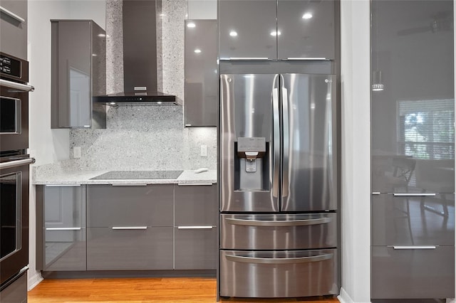 kitchen featuring tasteful backsplash, light stone counters, stainless steel appliances, wall chimney range hood, and gray cabinets