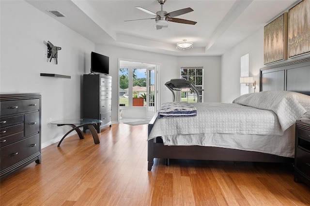 bedroom featuring ceiling fan, light hardwood / wood-style flooring, and a tray ceiling