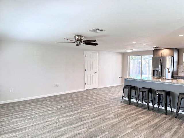 kitchen featuring sink, a kitchen bar, stainless steel refrigerator with ice dispenser, light stone countertops, and light hardwood / wood-style flooring