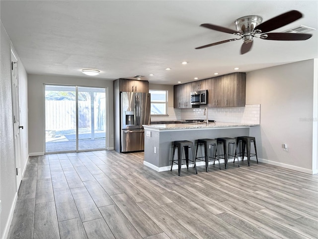 kitchen with a breakfast bar, stainless steel appliances, tasteful backsplash, light hardwood / wood-style floors, and kitchen peninsula