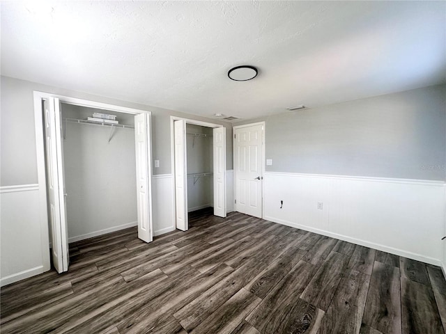 unfurnished bedroom with dark hardwood / wood-style floors, a textured ceiling, and two closets