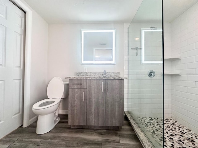 bathroom with vanity, hardwood / wood-style flooring, toilet, and tiled shower