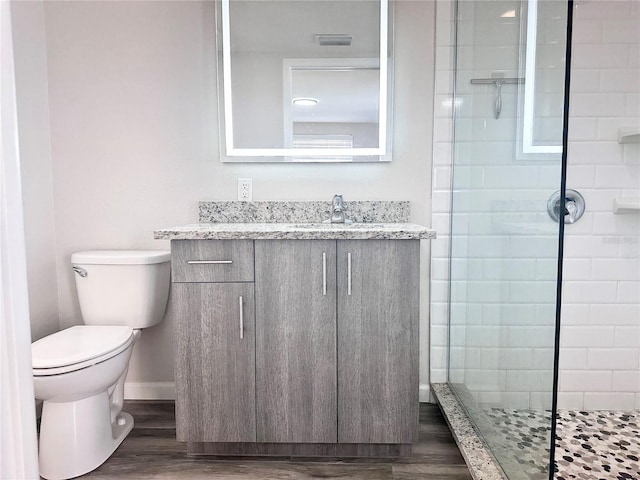 bathroom featuring vanity, tiled shower, hardwood / wood-style floors, and toilet