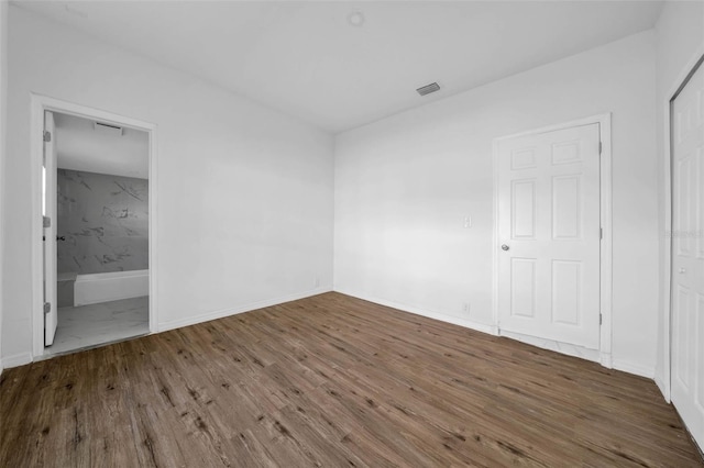 unfurnished bedroom with connected bathroom and dark wood-type flooring