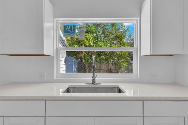 kitchen featuring light stone countertops, white cabinetry, a wealth of natural light, and sink