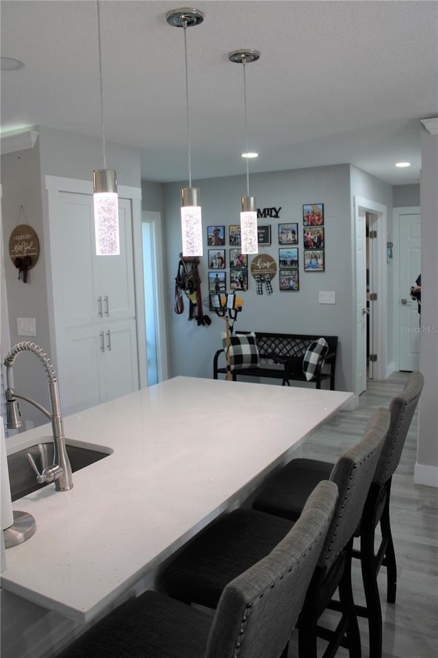 kitchen with light wood-style flooring, a kitchen breakfast bar, light countertops, pendant lighting, and a sink