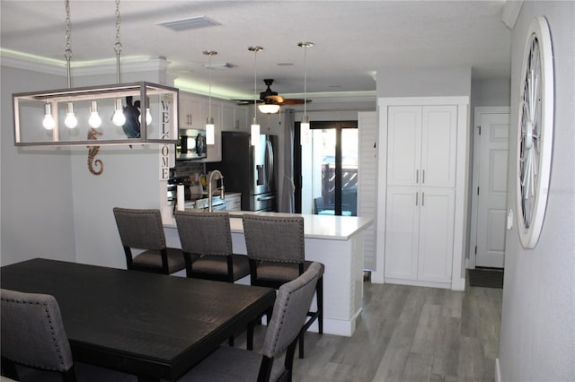 dining room with light wood-style floors, ceiling fan, visible vents, and ornamental molding